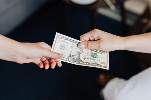 Two hands exchanging a ten dollar bill as a tip