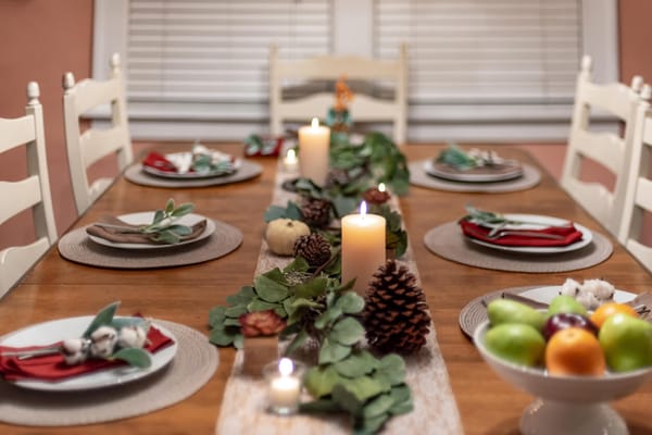 Wooden dining table set for a holiday dinner with candles, pine cones and a eucalyptus runner