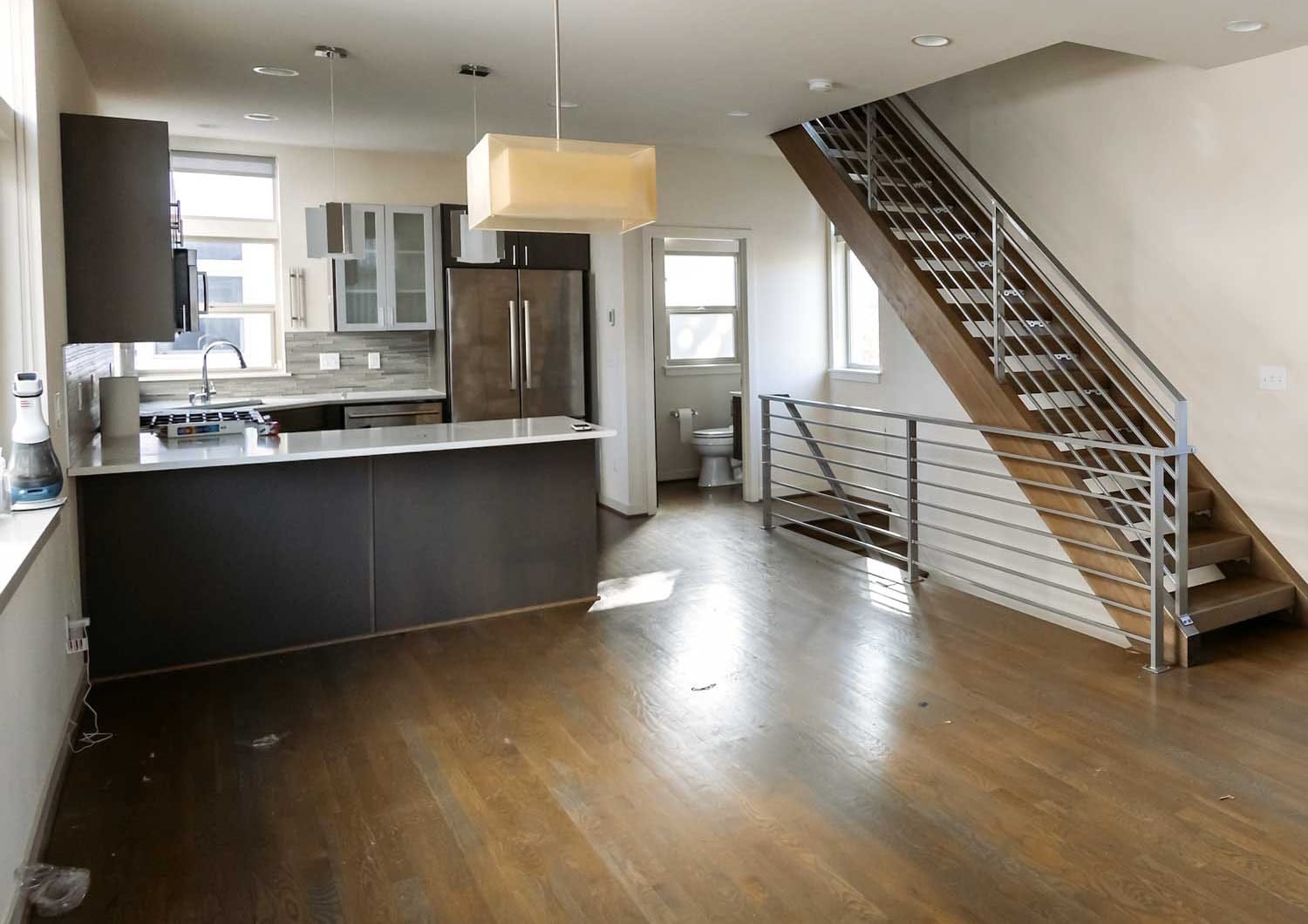 Before image of a Ballard Seattle tri-level townhouse during move-out, showing an unclean living room, kitchen counters, and modern staircase before professional cleaning.