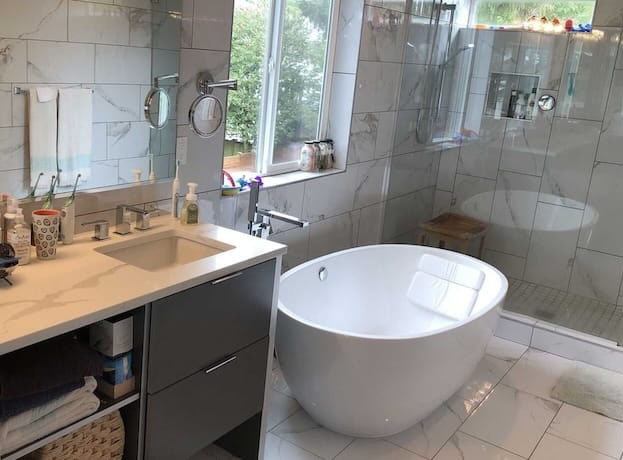 Spotless and organized modern master bathroom with marble-look tiles, shiny glass shower doors, clean floating bathtub, and neatly arranged countertops after professional deep cleaning in Bellevue.