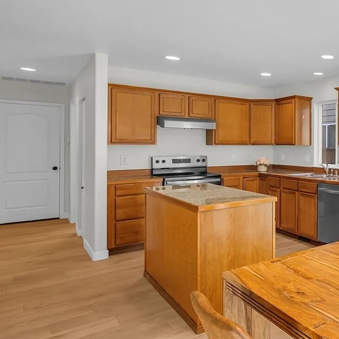 Clean kitchen with wood cabinets, an island, stainless range and light wood floors