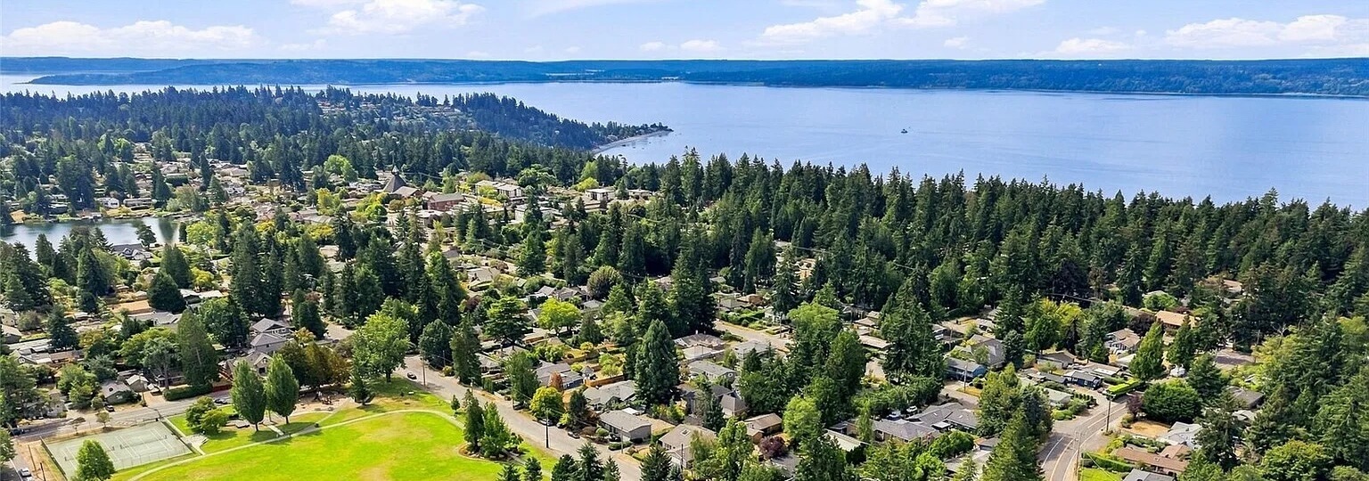 Aerial view of Burien homes among tall evergreens with Puget Sound and a forested shoreline beyond
