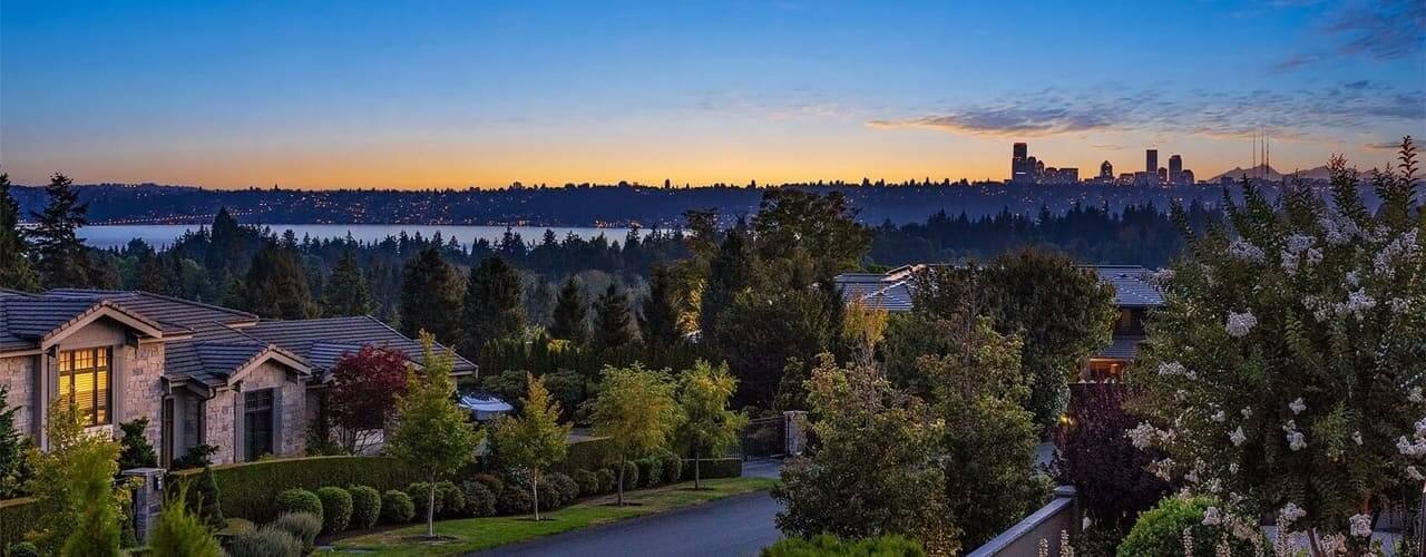 Clyde Hill homes and trees at dusk with Lake Washington and the Seattle skyline across the water