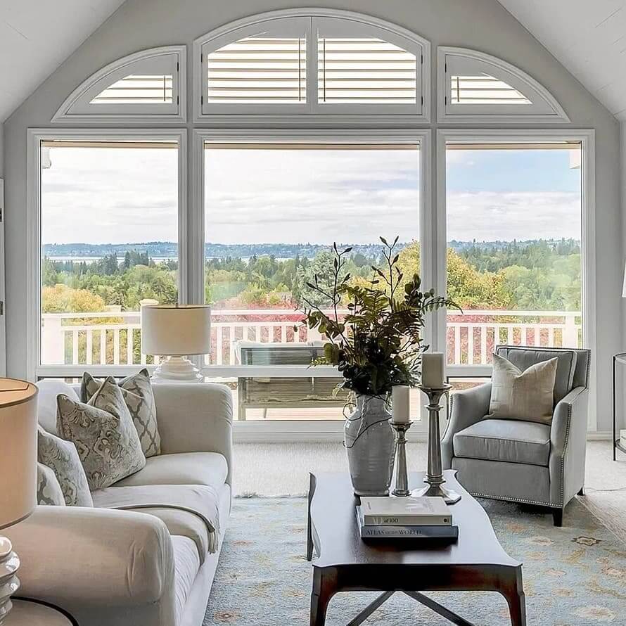 Bright vaulted living room with arched windows, cream sofa and armchair facing a treetop view