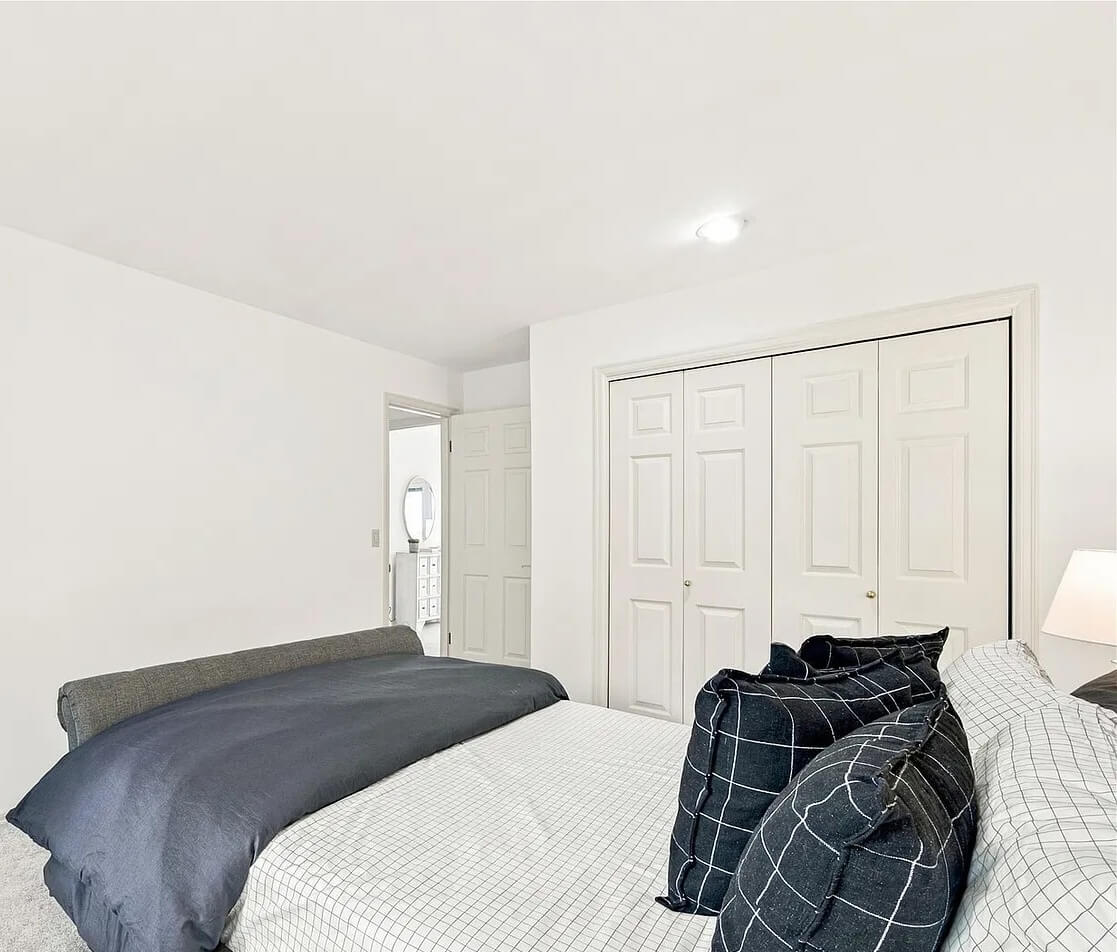 Clean, bright bedroom with a made bed, white closet doors and light carpet