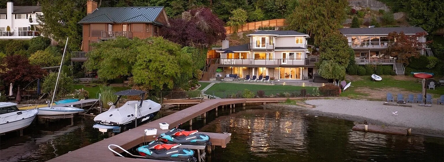 Lake Washington waterfront homes with a long private dock, boats and tall evergreens at dusk