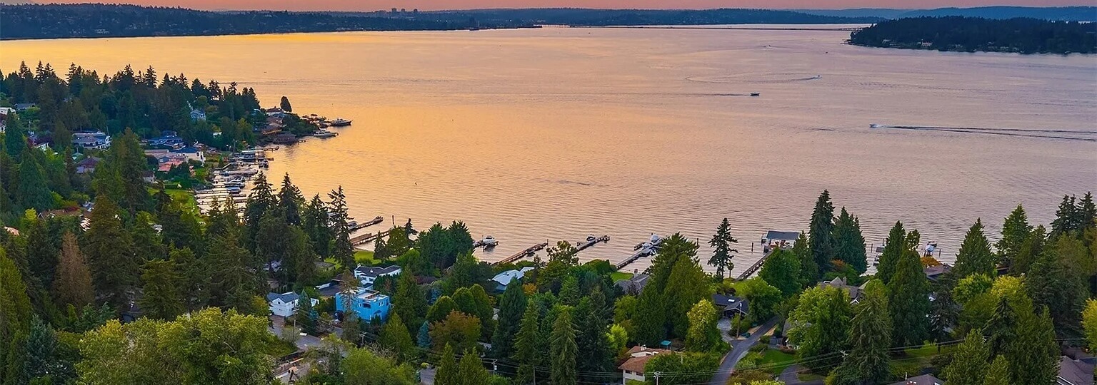 Aerial sunset view of Mercer Island waterfront homes, private docks and tall evergreens on Lake Washington