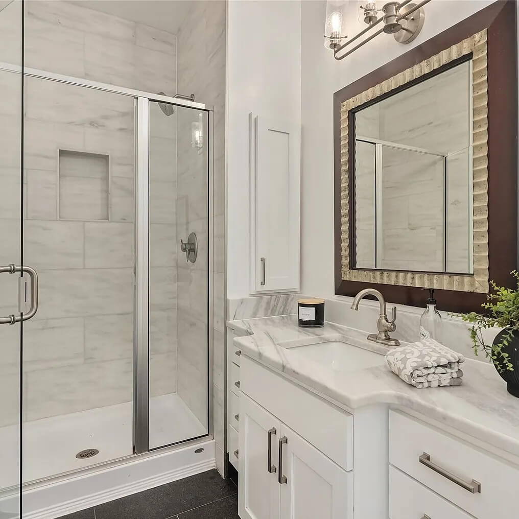 Spotless bathroom with a marble vanity, white cabinets, framed mirror and glass walk-in shower