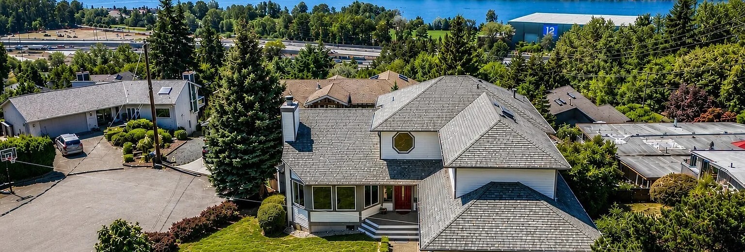 Aerial view of a two story Newcastle home among tall evergreens, with Lake Washington in the distance