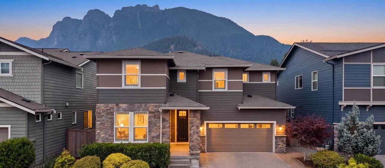 Craftsman style homes with warm lit windows at dusk, with the rocky face of Mount Si behind them