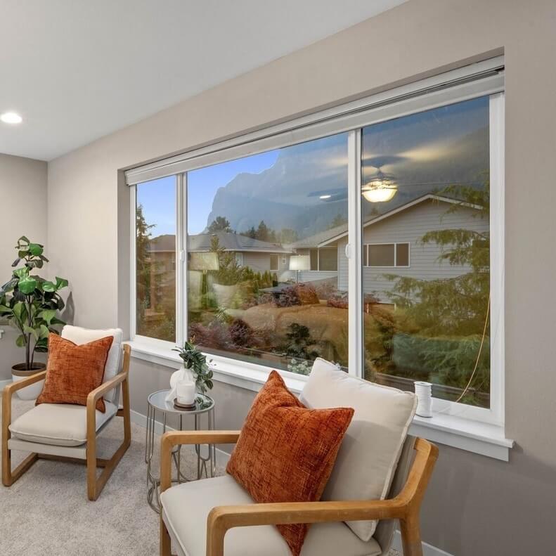 Bright sitting area with two wood armchairs, orange pillows and a large window looking out toward Mount Si