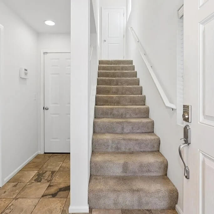 Clean entryway with a carpeted staircase, white doors and walls, and a stone tile floor