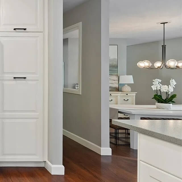 Clean white kitchen with a speckled counter and hardwood hallway leading to a bright dining room