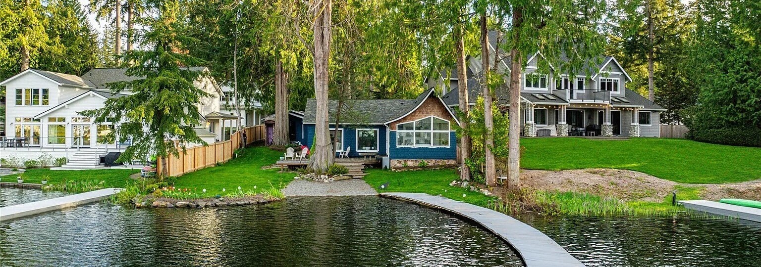 Lakefront homes with green lawns, tall evergreens and a curved walkway over the water in Sammamish