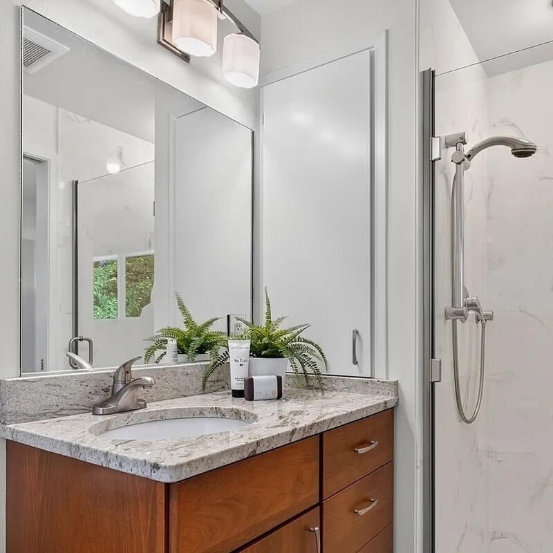 Clean bathroom with a granite vanity, wood cabinet, large mirror and glass walk in shower