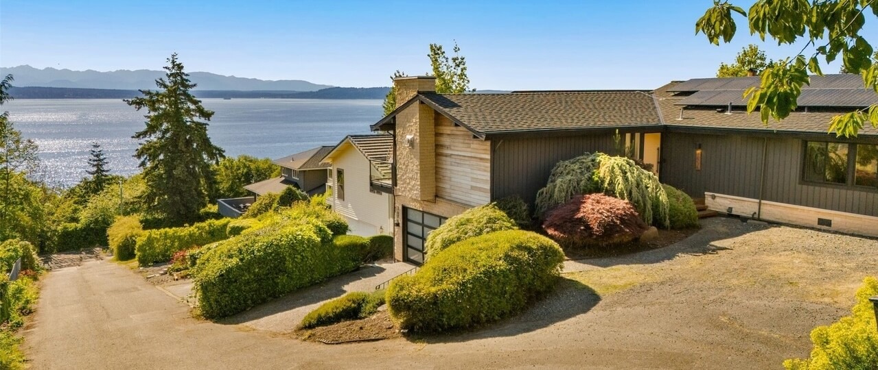 Modern hillside home with gray siding and landscaped hedges above Puget Sound, Olympic Mountains beyond