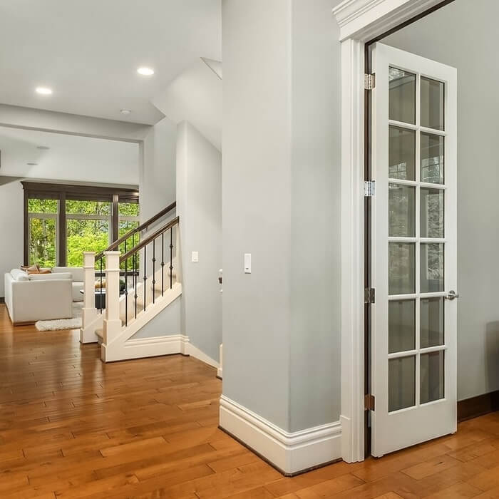 Bright entry hall with hardwood floor, a glass French door and a staircase, with a view to the living room