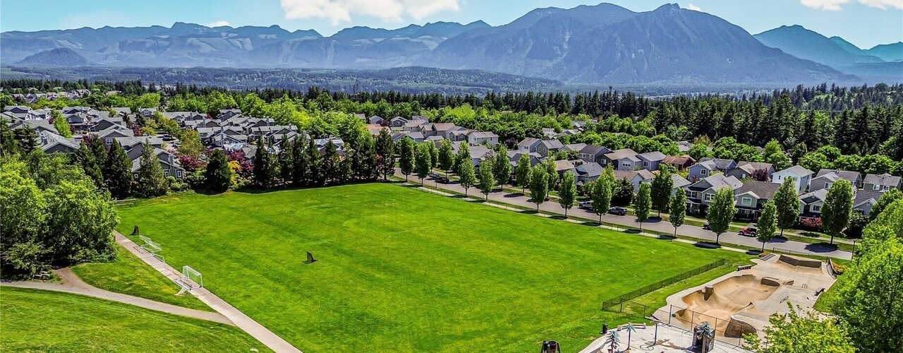 Aerial view of Snoqualmie Ridge homes along tree-lined streets beside a park, with Mount Si behind