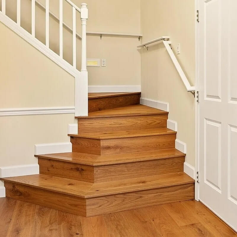 Hardwood staircase and matching wood floor in a clean entryway with white railings and cream walls