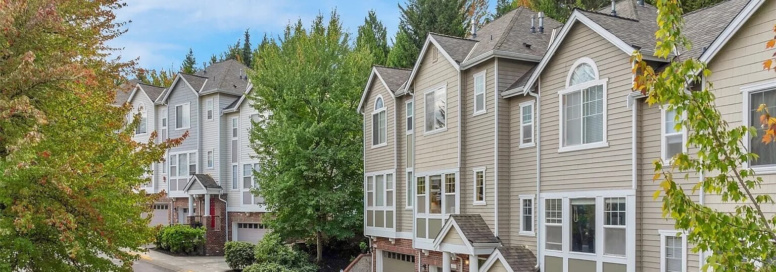 Row of three story townhomes with gray siding and garages among green and autumn trees in Woodinville