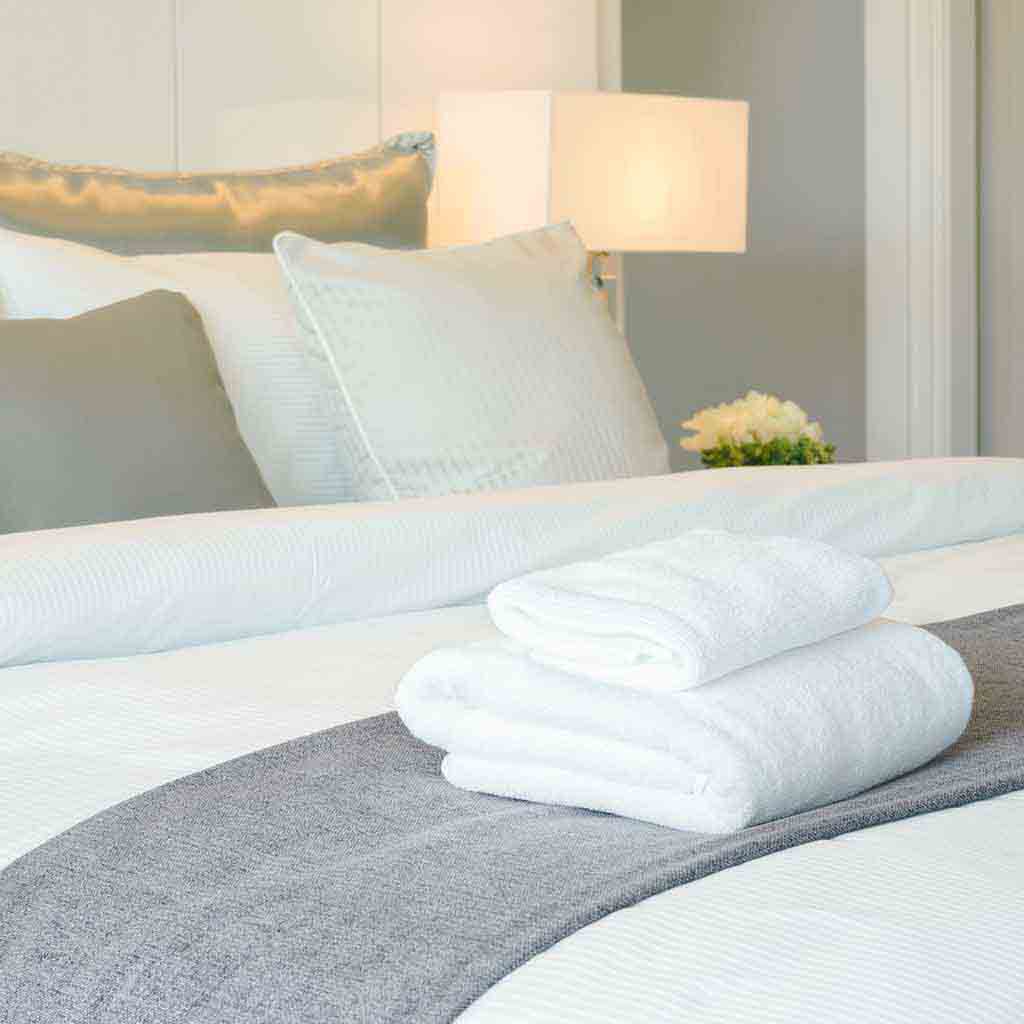 A well-made bed with fresh linens in a clean, neutral guest room, prepared for incoming guests as part of professional hospitality cleaning in Seattle