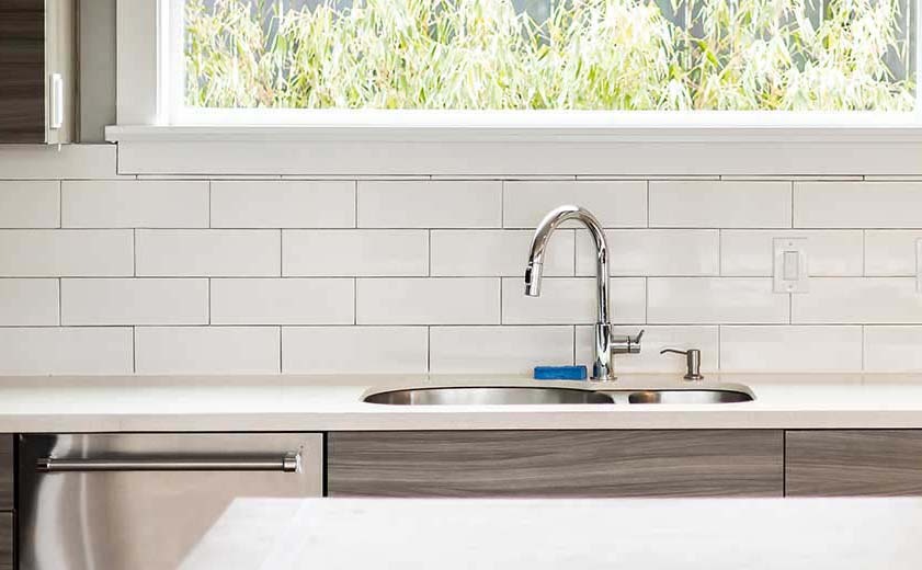 Spotless kitchen sink and polished chrome faucet with clean subway tile backsplash after apartment move-out cleaning in Seattle by Simply Clean