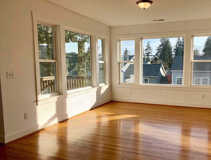 Clean empty room with gleaming hardwood floors and large windows overlooking a Seattle neighbourhood after apartment move-out cleaning by Simply Clean — prepared for final walkthrough and key handover