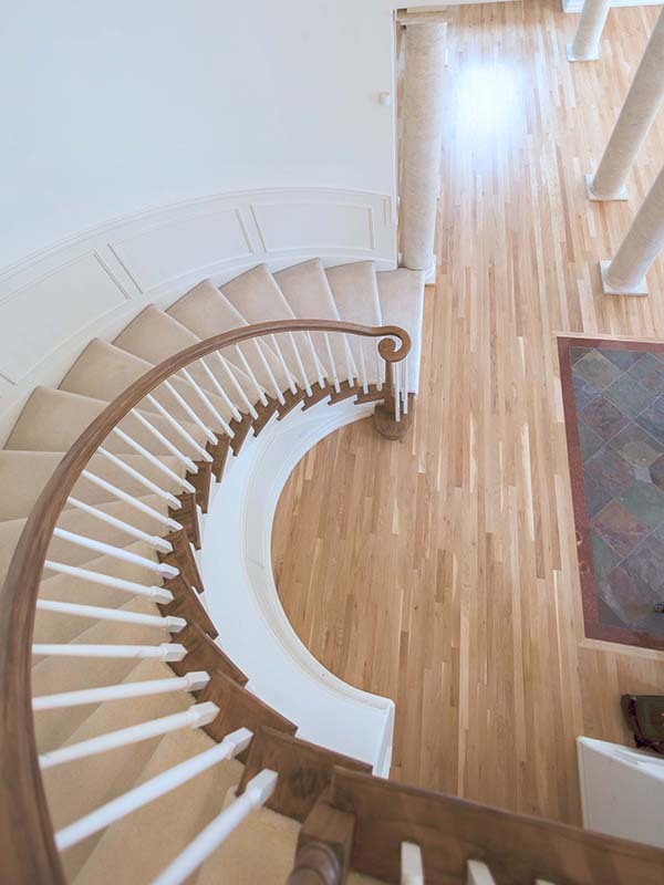 Spiral staircase with carpeted treads and hardwood floors below after move-out cleaning in a Seattle home by Simply Clean — viewed from above showing clean banister, white spindles, and gleaming hardwood