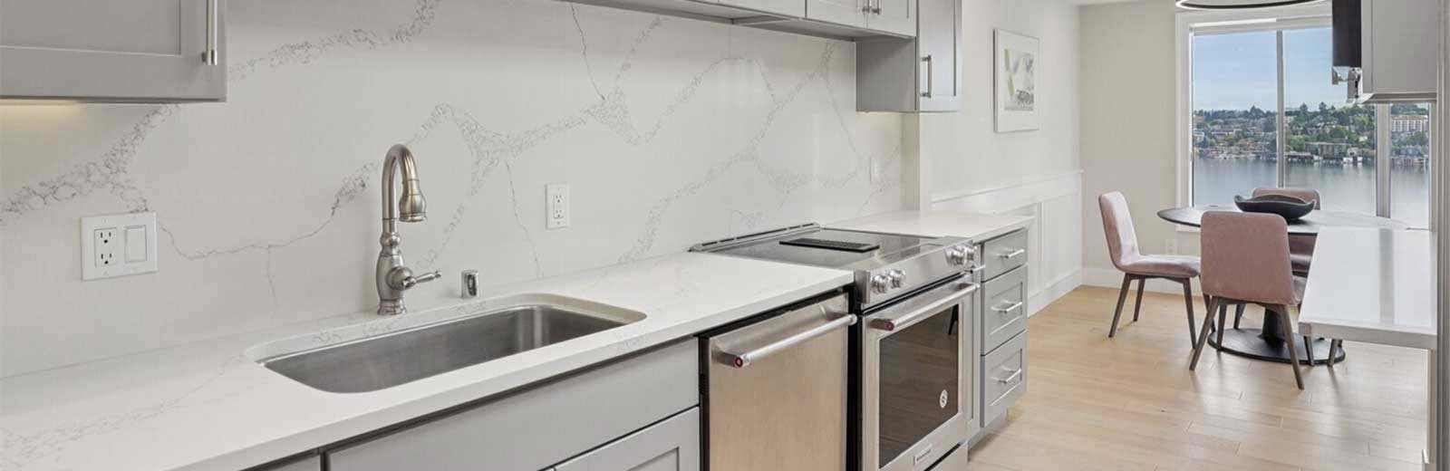 Newly renovated Seattle kitchen with marble slab backsplash, grey shaker cabinets, and stainless appliances after post-remodel cleaning by Simply Clean